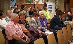 Eine Gruppe von Menschen verschiedenen Alters sitzt in Stühlen, wahrscheinlich in einem Besprechungsraum. Sie scheinen etwas zu hören.