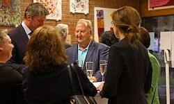Eine Gruppe formell gekleideter Menschen unterhält sich in einer Inneneinrichtung mit Wein glasses und Kunstwerken an den Wänden.