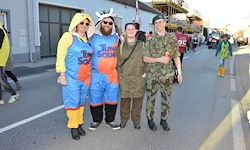 Vier Personen posieren für ein Foto auf einer Stadtstraße. Drei sind in Kostümen. Einer ist Soldat, ein anderer Pirat und der dritte ein Huhn.