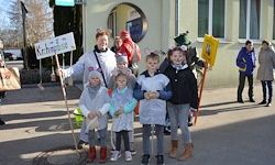 Eine Gruppe von Kindern in Regenmänteln, die Schilder halten und vor einem Gebäude für ein Foto posieren.