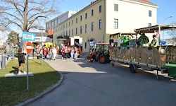 Ein geschmückter Paradewagen fährt die Straße hinunter, mit Menschen, die auf dem Bürgersteig stehen, in der Nähe eines Gebäudes mit mehreren Fenstern.
