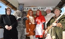 Eine Gruppe von Menschen in verschiedenen Kostümen, darunter ein Wolf, Rotkäppchen und andere, posiert für ein Foto vor einem Geschäft.