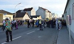 Eine Menschenmenge in Kostümen versammelt sich auf der Straße in der Nähe von Gebäuden, einige gehen und andere stehen.