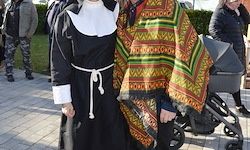 Eine Nonne und eine Person in einem bunten Poncho stehen nebeneinander auf einem Bürgersteig mit anderen Personen in der Umgebung.