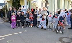 Eine Gruppe von Menschen, darunter Kinder in Kostümen, posiert für ein Foto vor einem Gebäude mit einem Mann in einem Bärenkostüm.