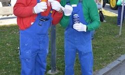 Zwei Menschen in Videospielkostümen stehen draußen auf dem Rasen. Einer hält ein Getränk, der andere eine Flasche.