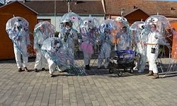 Eine Gruppe von Menschen in weißen Kostümen mit durchsichtigen Regenschirmen steht vor einem Gebäude.