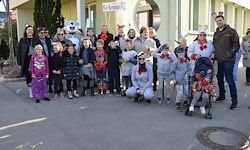 Eine Gruppe von Menschen, einige in Kostümen, posiert für ein Foto auf einer Straße vor einem Gebäude.