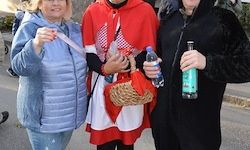 Drei Menschen auf der Straße, eine als Rotkäppchen verkleidet, eine andere in Schwarz und eine Frau in Blau, die eine Flasche hält.