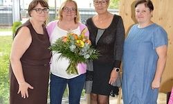 Vier Frauen stehen zusammen, eine hält einen Blumenstrauß. Sie alle lächeln und scheinen für ein Foto zu posieren. Der Hintergrund zeigt einen Rasenbereich.