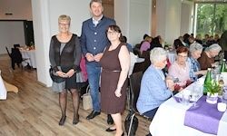 Eine Gruppe von Menschen, darunter drei Frauen und ein Mann, stehen in einem Restaurant und posieren für ein Foto. Sie befinden sich in der Nähe eines Tisches mit Flaschen und Gläsern.