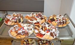 Ein Metalltablett hält mehrere Teller mit Desserts mit Toppings wie Erdbeeren, Schlagsahne und Schokolade. Die Desserts umfassen Kuchen, Croissants und andere Gebäcke.