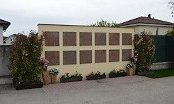 Eine Wand mit zahlreichen Plaketten, umgeben von Pflanzen und Blumen, steht vor einem Haus.