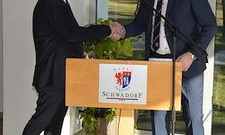 Zwei Männer in Anzügen schütteln sich die Hände vor einem Podium mit dem Wort Schwarzwald darauf, einer Pflanze und einem Mikrofon.
