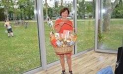 Eine Frau in einem orangefarbenen Shirt hält einen Korb mit Snacks vor einer Glastür mit Blick auf ein Grasfeld.