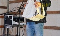 Ein Mann spielt Akkordeon auf der Bühne mit einem Mikrofon vor ihm, neben einem Keyboard.