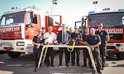 Eine Gruppe von Feuerwehrleuten steht vor Feuerwehrfahrzeugen. Sie tragen Uniformen und posieren für ein Foto.