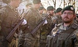 Eine Gruppe Soldaten in Tarnuniformen, die Gewehre halten, steht in einer Reihe im Freien. Einige tragen Barette, und sie scheinen auf einer Mission zu sein.