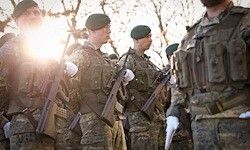 Militärangehörige in Tarnuniformen stehen in Formation und halten Gewehre. Die helle Sonneneinstrahlung beleuchtet die Szene, und sie tragen grüne Barette und weiße Handschuhe.