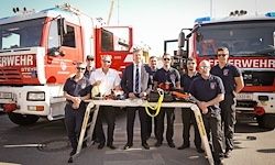 Eine Gruppe von Feuerwehrleuten steht hinter einem Tisch vor Feuerwehrwagen und posiert für ein Foto.