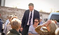 Ein Mann in einem Anzug und Krawatte geht durch eine Gruppe von Menschen. Eine Frau mit einem Leopardenmuster-Oberteil hebt ihre Hand.