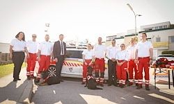 Eine Gruppe von Menschen in roten Uniformen und einem Hund steht vor einem Krankenwagen.