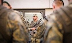 Eine Gruppe von Soldaten in Tarnuniformen, wobei ein Soldat ein Gewehr hält und den anderen im Raum Anweisungen gibt.