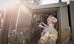 Zwei Soldaten in Militäruniformen arbeiten in einem Militärfahrzeug, einer justiert Ausrüstung. Das Fahrzeug ist offen, und Sonnenlicht scheint hinein.