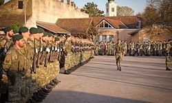 Eine Militärparade vor einem Gebäude mit Soldaten in grünen Uniformen, die in Formation marschieren, und einem Offizier, der im Vordergrund führt.