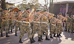 Eine Marschkapelle von Soldaten in Tarnuniformen spielt Blechblasinstrumente bei einer Parade an einem sonnigen Tag.