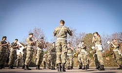Eine Gruppe von Militärangehörigen in Tarnuniformen, die in Formation stehen und an einem klaren Tag mit Instrumenten auftreten.