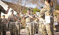 Eine Gruppe von Militärmusikern in Tarnuniformen spielt im Freien und spielt verschiedene Instrumente wie Flöten und Trommeln.