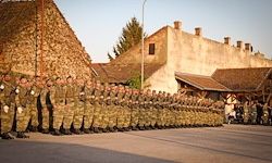 Eine große Gruppe von Militärangehörigen in Tarnuniformen steht in Formation vor historischen Gebäuden unter klarem Himmel.