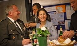 Eine Gruppe von Menschen sitzt um einen Tisch mit Bierflaschen und Gläsern herum, lächelt und hat eine gute Zeit. Dahinter ist eine Pinnwand mit angehefteten Papieren.