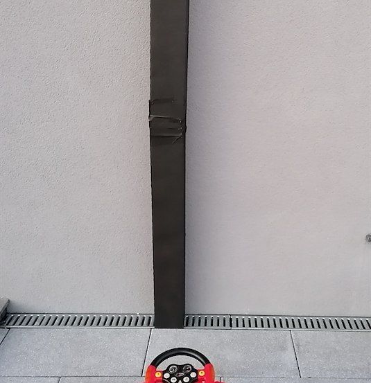 Ein rotes Spielzeugauto mit Lenkrad steht auf einem gefliesten Boden neben einer Wand mit einer Verkehrsampel-Aussparung.