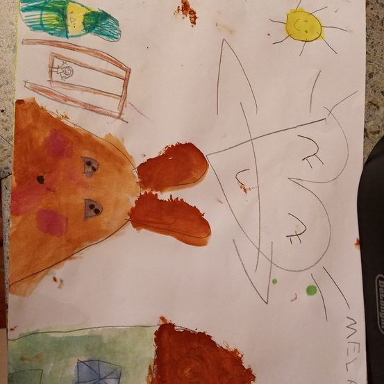 Eine Kinderzeichnung auf Papier zeigt ein braunes Tier mit großen Ohren, ein Haus mit einem Fenster und eine Sonne am Himmel.