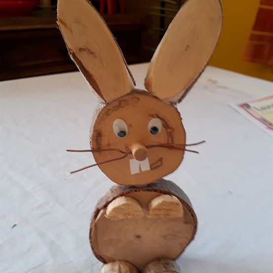 Eine hölzerne Spielzeugkaninchen mit großen Ohren und einem lächelnden Gesicht, das auf einer weißen Oberfläche steht.