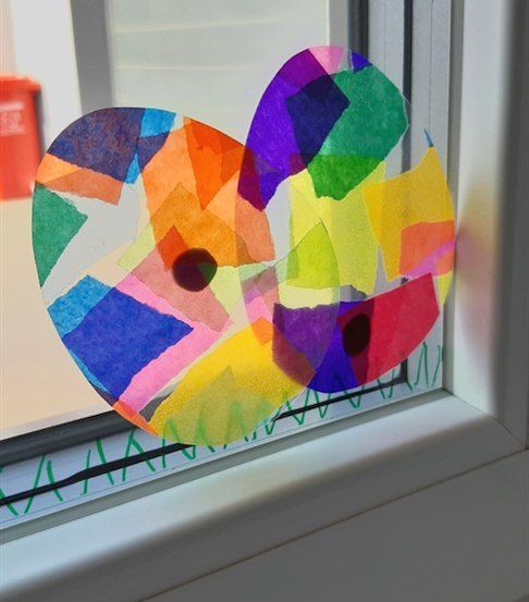 Ein farbenfrohes herzförmiges Papiercollage ist an einem Fenstersims befestigt. Das Herz besteht aus verschiedenen farbigen Papierstücken und schafft eine lebendige und künstlerische Darstellung.