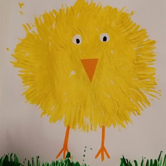 Ein handgemaltes Küken mit leuchtend gelben Federn, großen weißen Augen und einem orangefarbenen Schnabel steht auf einem weißen Hintergrund mit grünem Gras darunter.