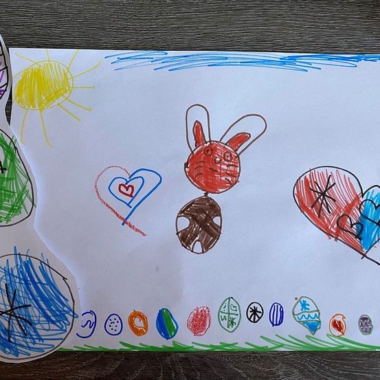 Eine Kinderzeichnung auf einem weißen Blatt mit einem roten Hasen, einer gelben Sonne und verschiedenen farbigen Herzen und Symbolen.