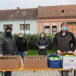 Vier Personen mit Mundschutz stehen hinter einem Tisch mit Kisten voller Produkte. Eine Person hält eine Kiste mit Äpfeln.