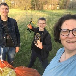 Drei Menschen stehen auf einem Rasen und posieren lächelnd für ein Foto. Eine Frau mit Brille ist rechts, ein Junge mit einem Hammer in der Mitte und ein Mann links. Sie halten Säcke mit Müll.