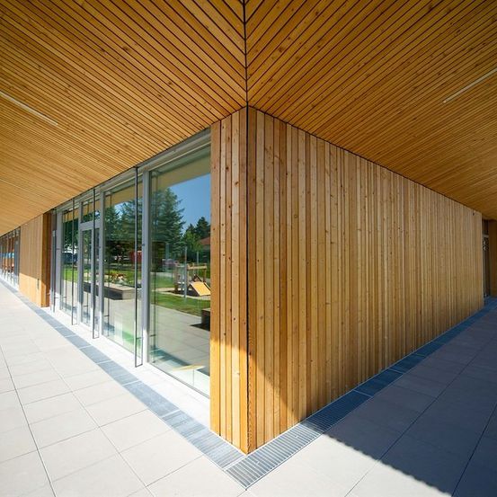 Ein modernes Gebäudeaußen mit Holzpaneelen und Glasfenstern, reflektiert Bäume und einen Rasenbereich.