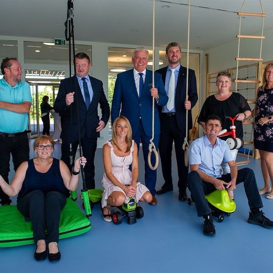 Eine Gruppe von Menschen in formeller Kleidung posiert für ein Foto in einem Raum mit Trainingsgeräten.