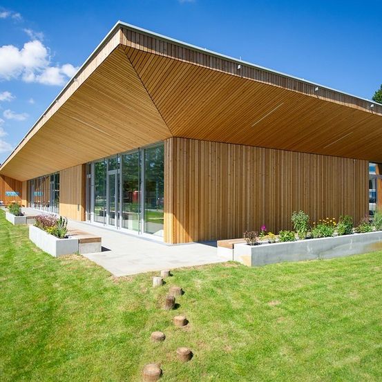 Ein modernes Gebäude mit Holzaußenwänden und Glasfenstern, umgeben von einem gepflegten Rasen und Garten.