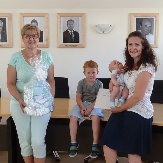Zwei Frauen und zwei Kinder posieren für ein Foto in einem Büro. Eine Frau hält ein Baby und die andere eine Tüte mit Windeln. Ein Junge sitzt auf einem Schreibtisch.