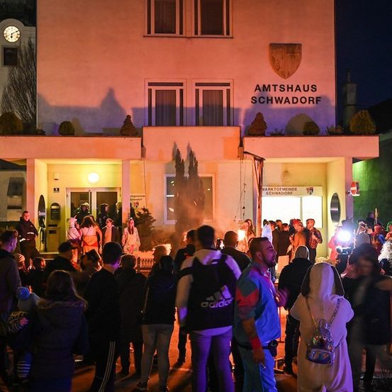 Eine Menschenmenge in Kostümen und mit Lichtern versammelt sich bei Nacht vor dem Amtshaus Schwadorf.