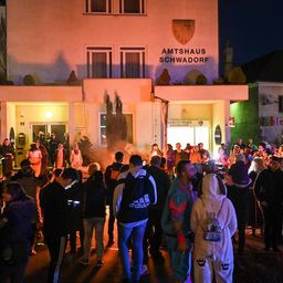 Eine Menschenmenge versammelt sich bei Nacht vor dem Amtshaus Schwadorf, einige tragen Kostüme und Masken, und in der Mitte befindet sich ein Lagerfeuer.