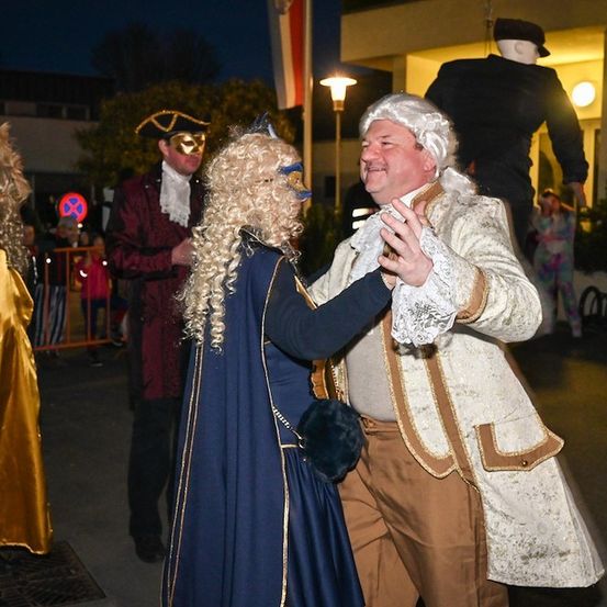 Ein Mann und eine Frau in Kostümen aus der Vergangenheit tanzen nachts vor einem Gebäude.