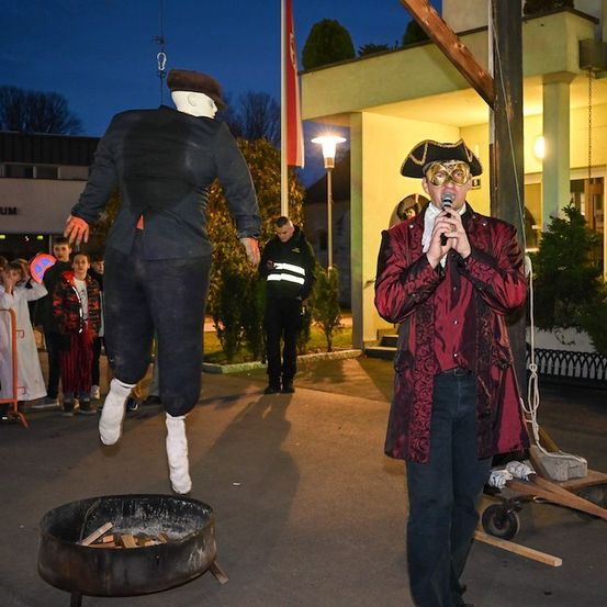 Ein Mann in einem Piratenkostüm spricht in ein Mikrofon, während ein Mannequin in einem schwarzen Anzug in einen Feuerkorb springt.